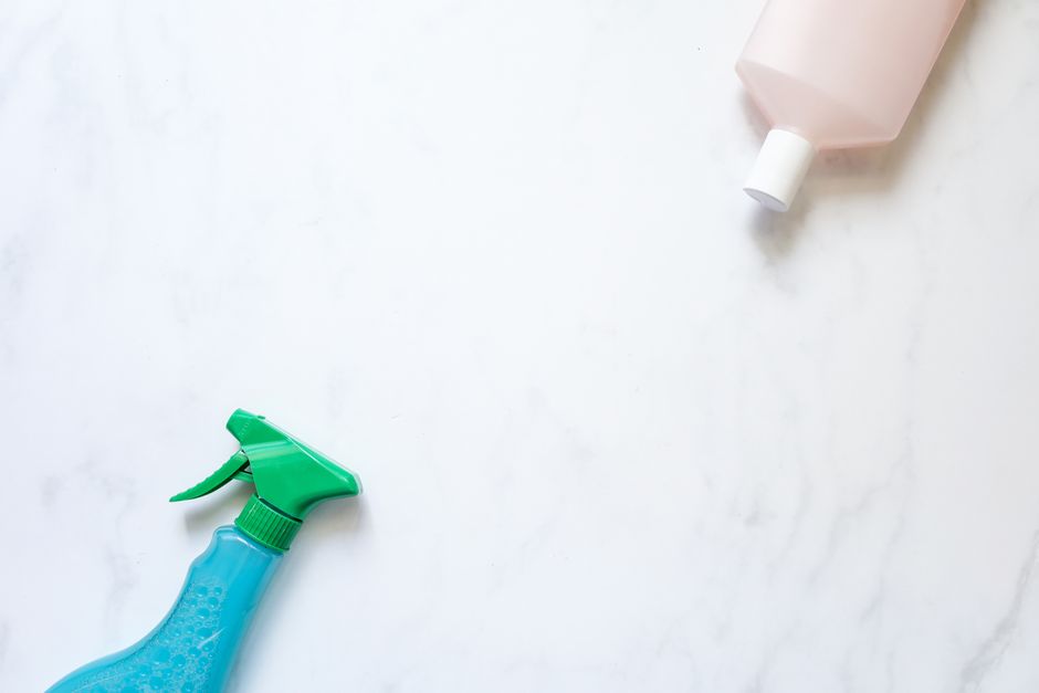 Flat lay of cleaning spray and bottle on a white surface with ample copy space.