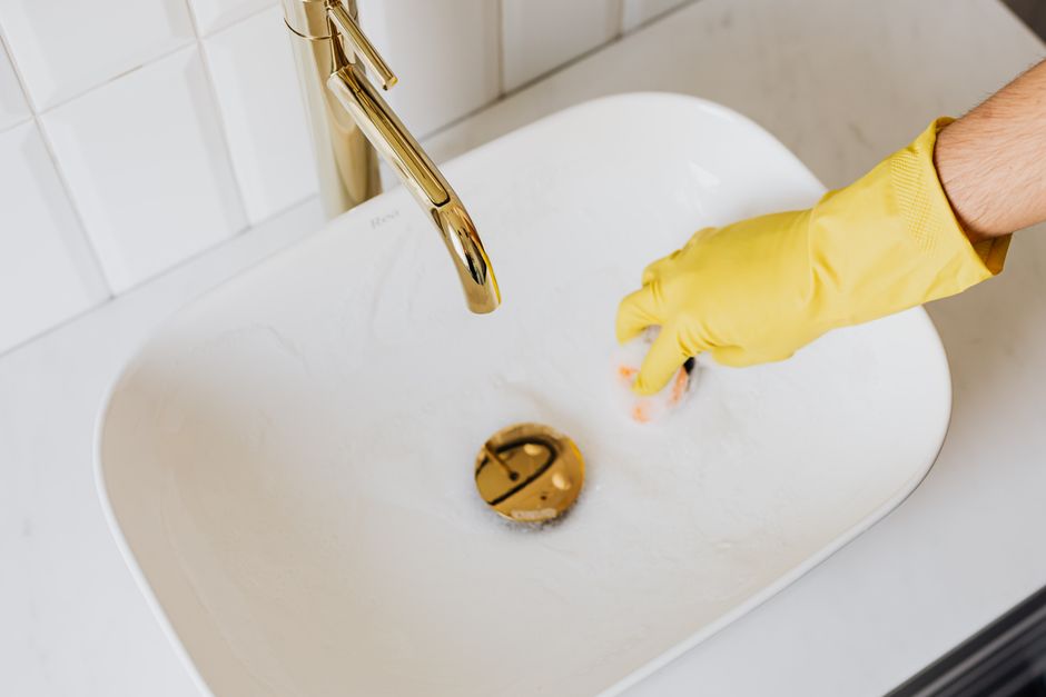 From above of crop anonymous person in yellow latex protective glove using sponge with detergent for cleaning sink in bathroom